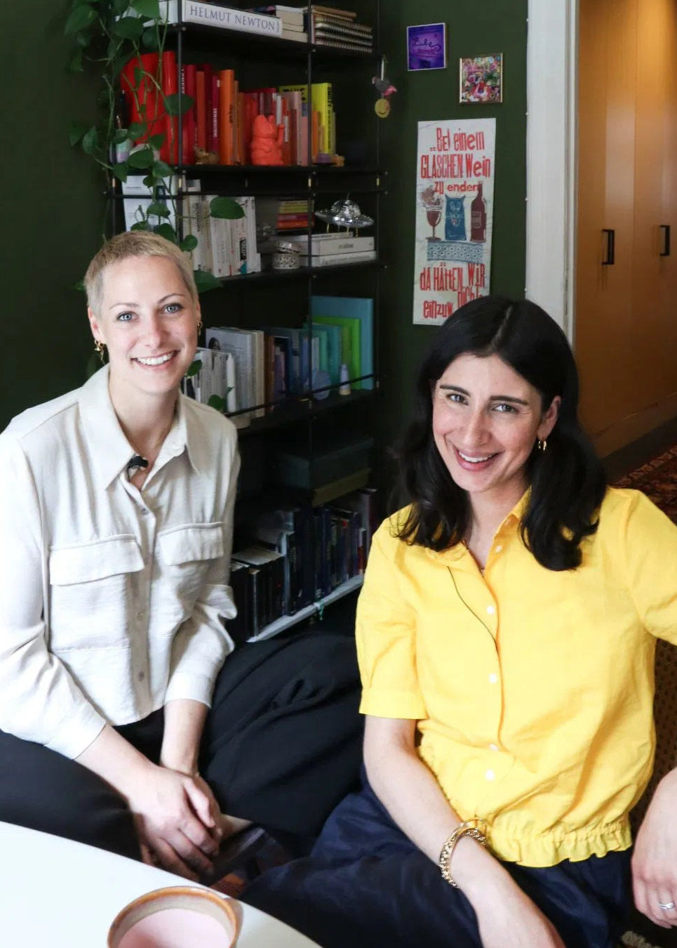 Two women sitting together in a room with green walls and bookshelves.